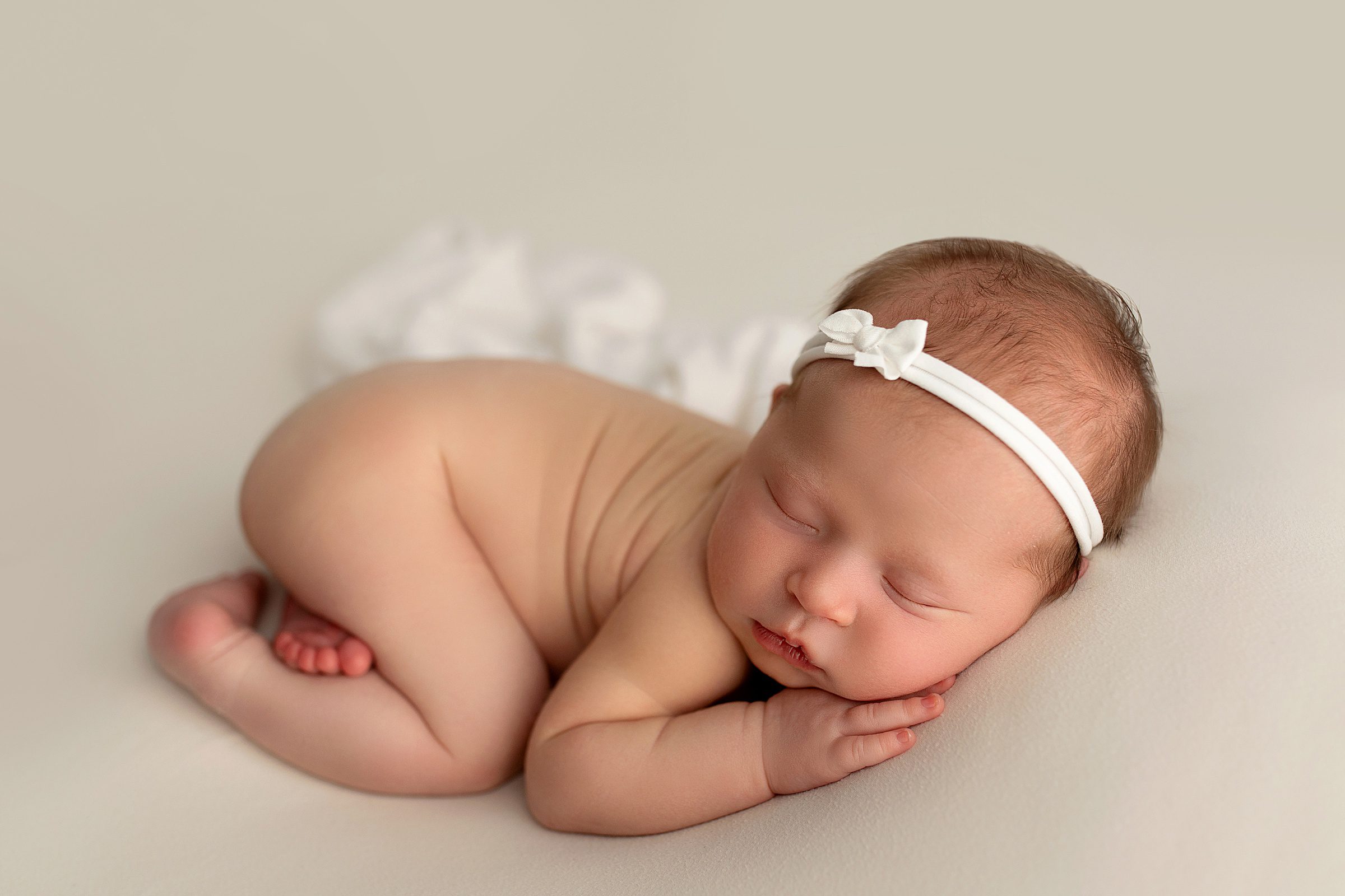 newborn baby girl with white bow on neutral backdrop during photo session in bentonville arkansas studio