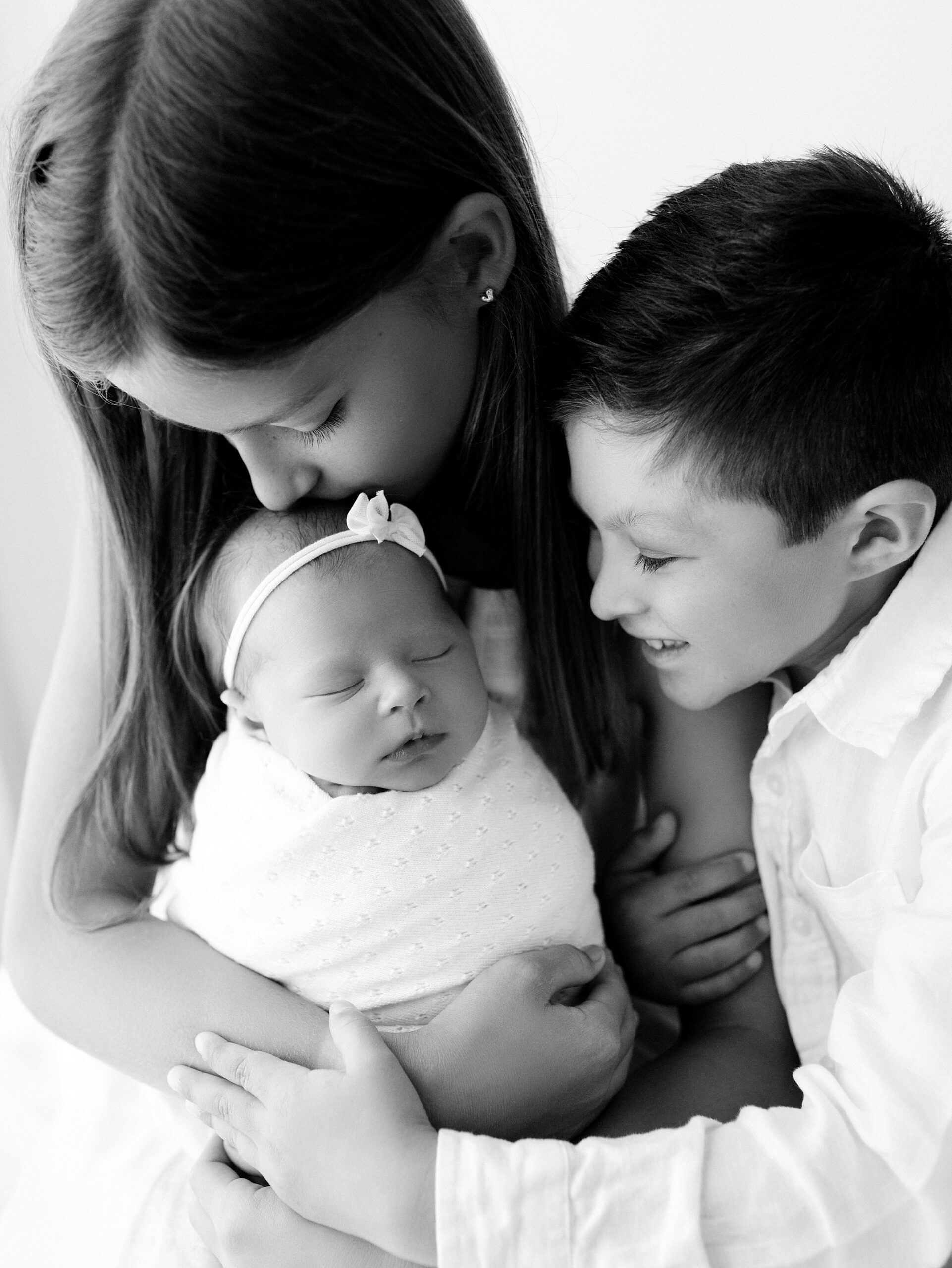 black and white photo of newborn baby with older siblings smiling during photoshoot in northwest arkansas