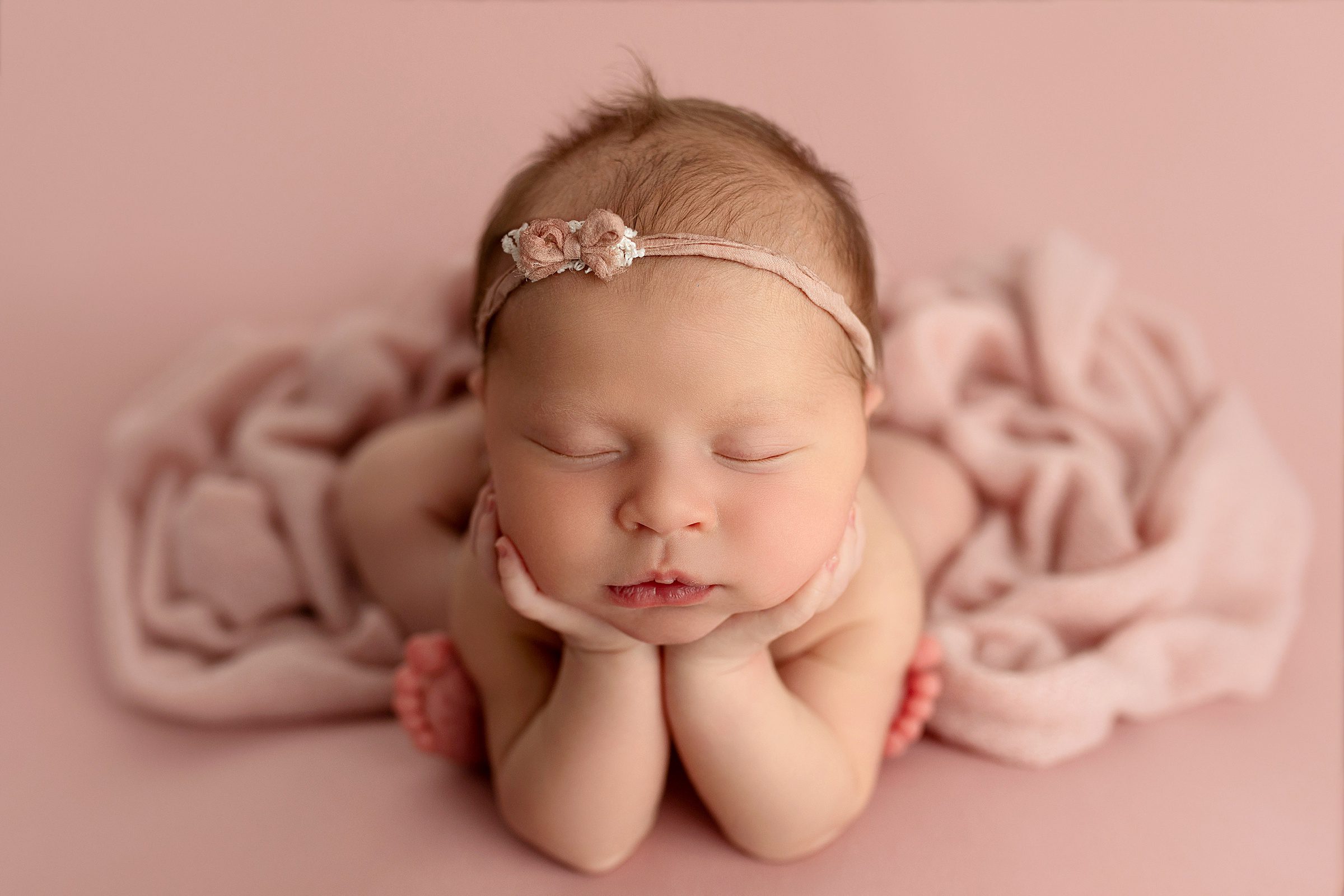 newborn baby girl in froggy pose on pink backdrop with tiny pink bow during newborn photography photo shoot in northwest arkansas studio